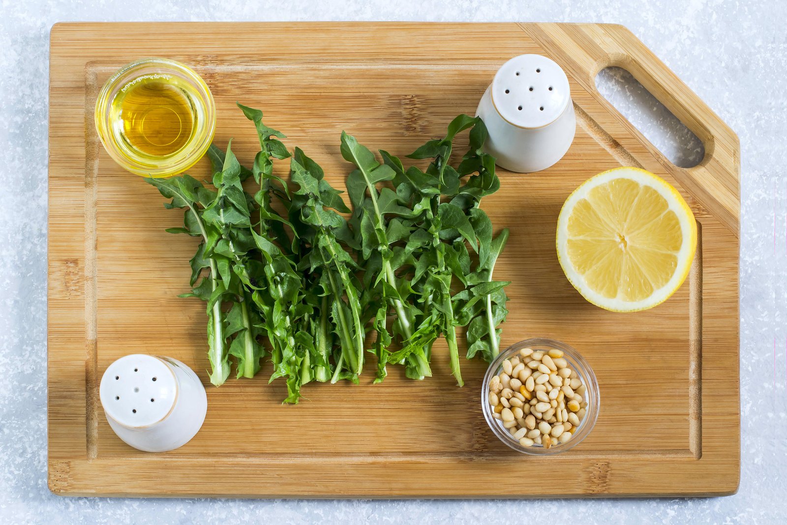 Ingredients for spring dandelion vitamin salad. Young leaves of dandelions, Siberian pine nuts, olive oil, lemon, salt and pepper on wooden cutting board. Spring food concept