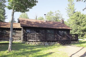  The main lodge at Mink Lake Wilderness Camp. Inside is a kitchen, dining area and seating area with chairs and  couches around a hearth fire place. | LINDEN FIGGIE