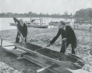 In August 1934, the Gunnarson family discovered a dugout canoe as they were extending their dock on North Arm Bay. The canoe has been dated to 1025-1165 A.D., making it the oldest dugout canoe found in Minnesota. Pictured here is G. A. and Helmer Gunnarson moving a canoe. | WESTERN HENNEPIN COUNTY PIONEER ASSOCIATION